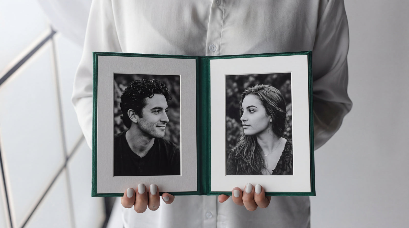 Two hands holding an open green folio, a black and white portrait set in each mat