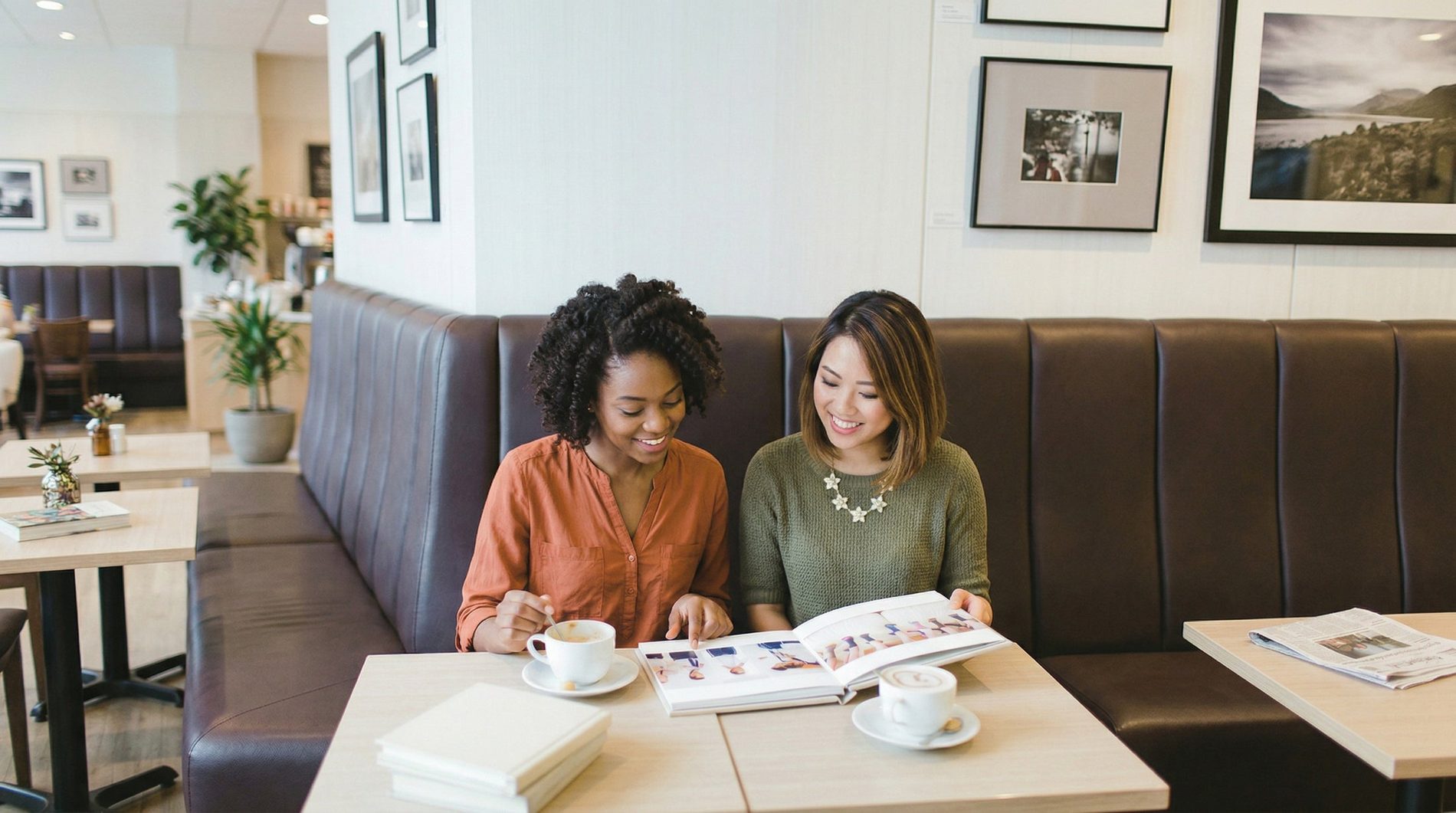 Two women smiling over an open wedding album at a cafe table