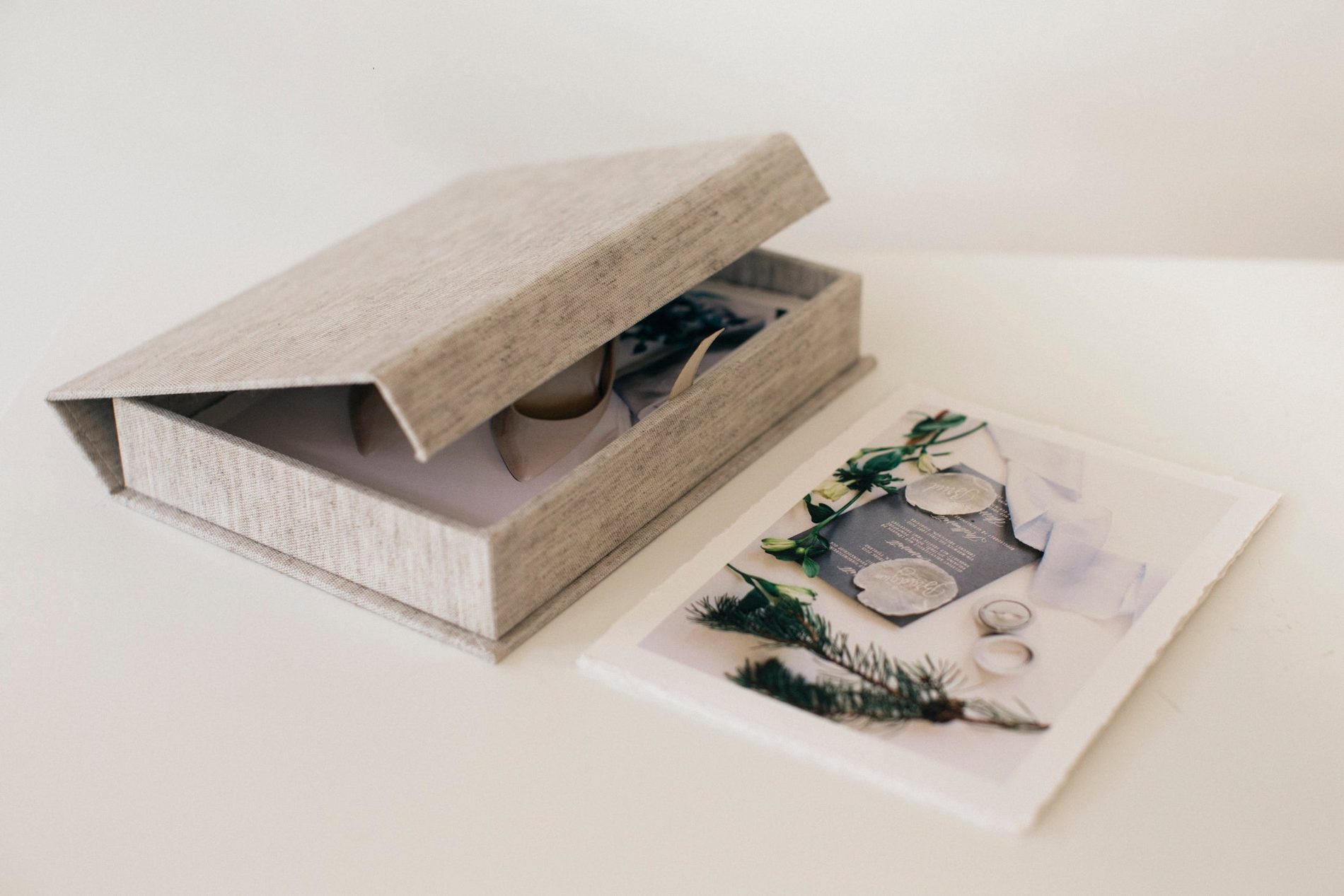 A linen clamshell box with the hinged lid open, a hand-deckled print lying beside it