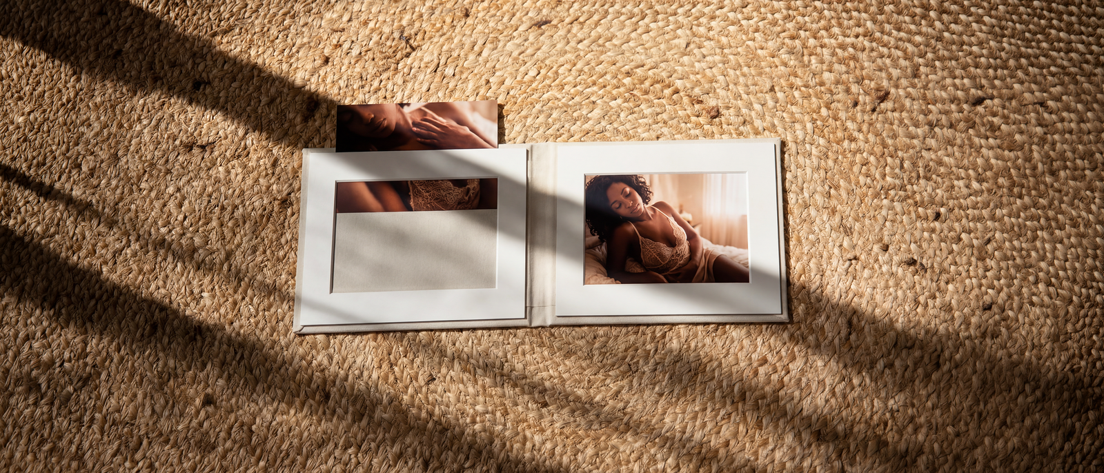 A folio open on a jute rug in low afternoon sun, boudoir prints set in cream mats