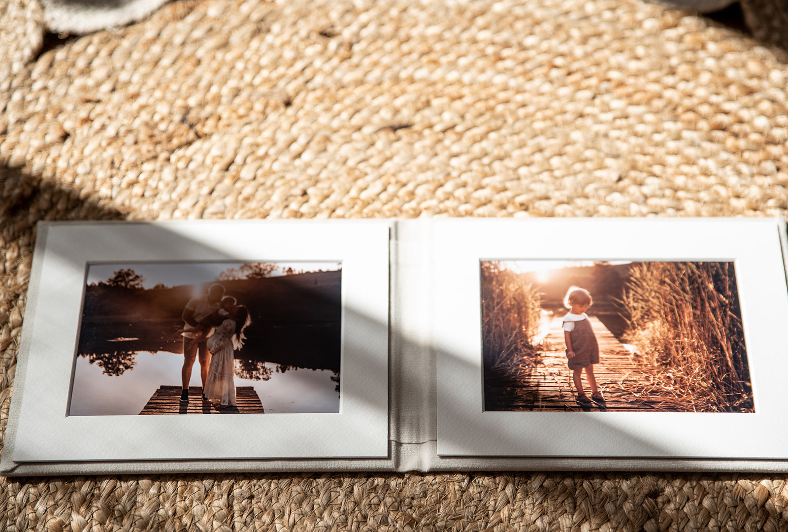 An open folio on a jute rug, two warm sunset family prints framed in white mats