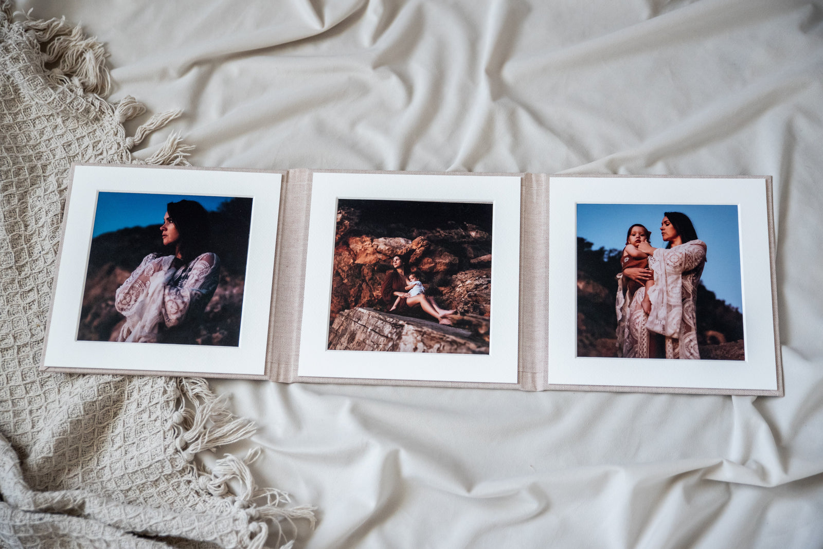 A self-mount folio opened flat on white linen, three square prints in cream mats