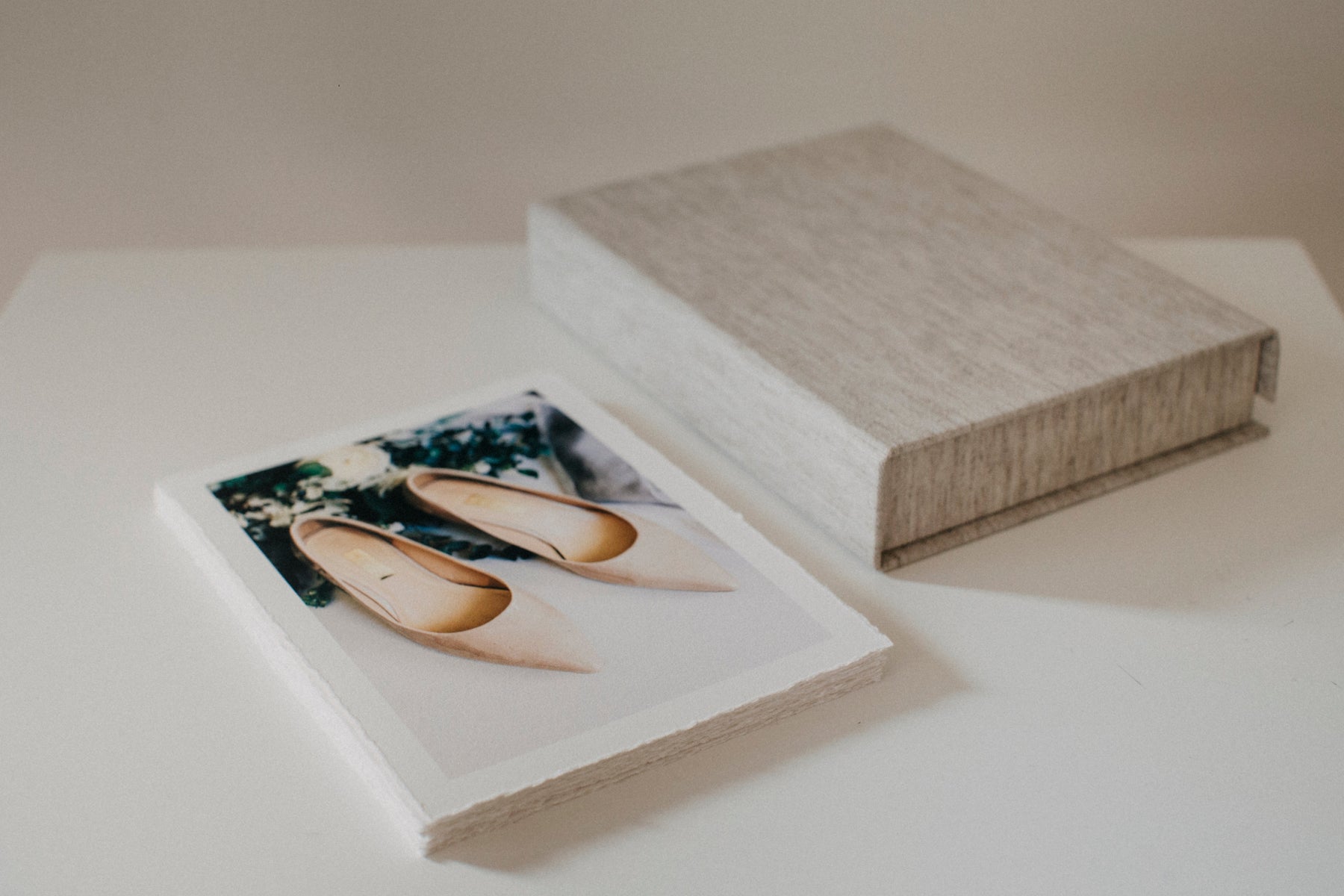 A closed linen print box on a white table next to a stack of prints with torn edges