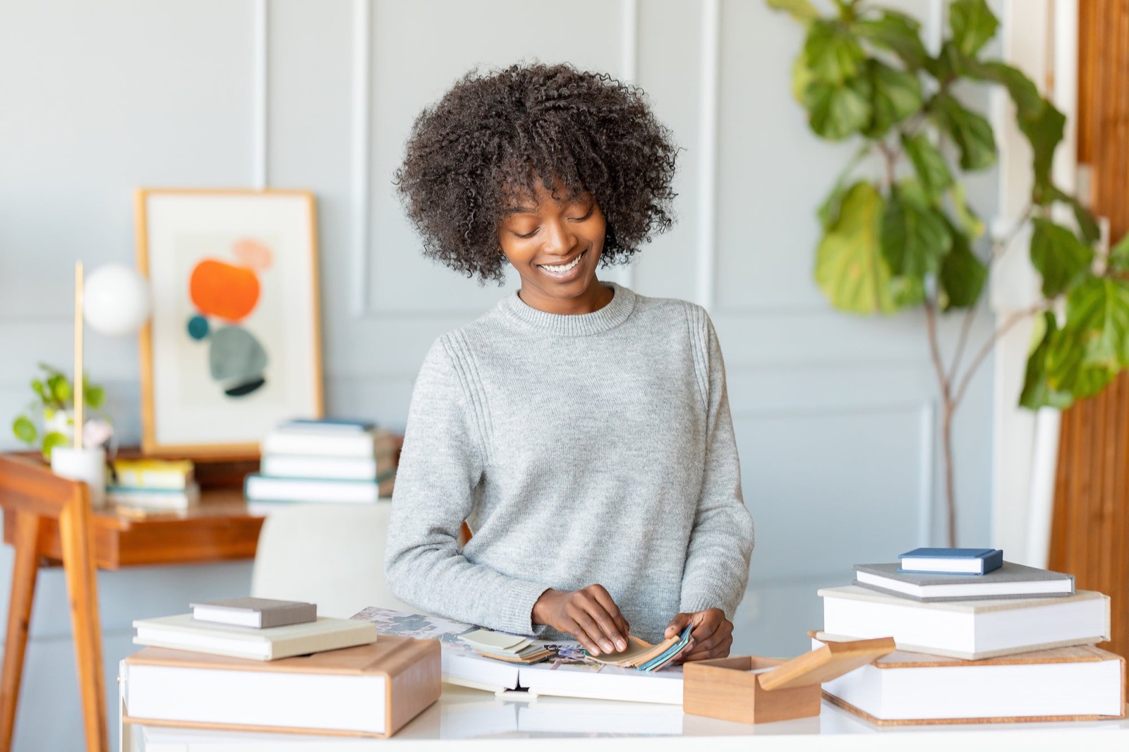 Photographer smiling as she looks through fabric swatches at her studio desk, album samples stacked around her