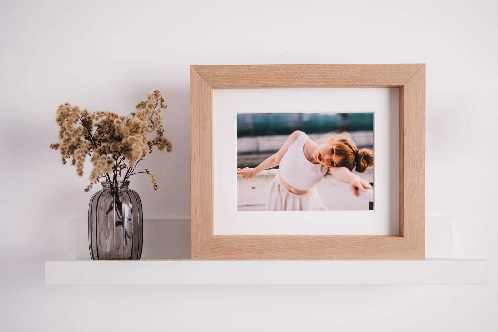 A light wood frame with a wide white mat, holding a portrait of a young dancer on a shelf